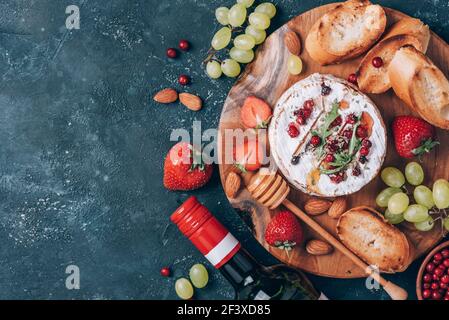 Serata romantica. San Valentino, concetto d'amore. Formaggio camembert al forno, miele, rucola, mirtillo, vino, pane tostato, uva, fragole, mandorla Foto Stock
