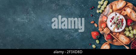 Formaggio camembert al forno con miele, rucola, mirtillo, pane tostato, uva, fragole, mandorle su fondo scuro. Vista dall'alto. Spazio di copia Foto Stock