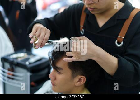 Barber rifinisce i capelli di un giovane uomo con le forbici nel suo barbiere Foto Stock