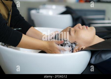 Il parrucchiere sta applicando lo shampoo e massaggiando i capelli di un cliente. L'uomo che ha i suoi capelli lavati in un parrucchiere. Foto Stock