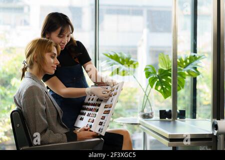 Asian parrucchieri donna stanno lasciando i clienti scegliere i colori dei capelli nei cataloghi in saloni di bellezza. Foto Stock