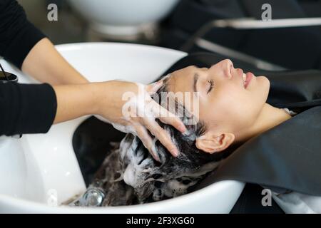 il parrucchiere sta applicando lo shampoo e massaggiando i capelli di un cliente. Donna che ha i suoi capelli lavati in un parrucchiere. Foto Stock