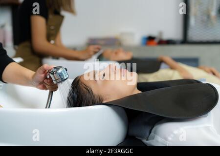 Il parrucchiere sta applicando lo shampoo e massaggiando i capelli di un cliente. Donna che ha i suoi capelli lavati in un parrucchiere. Foto Stock