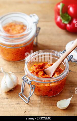 Condire il peperoncino rosso arrosto (Ajvar) in un vasetto con ingredienti Foto Stock