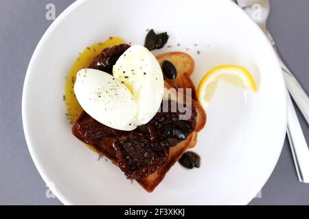 Colazione cibo. Uovo in camicia con tuorlo liquido su pane tostato con pomodori secchi. Foto Stock