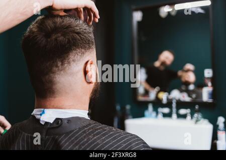 Barbiere, cliente maschile seduto in sedia mentre professionale parrucchiere fa i suoi capelli, vista posteriore. Foto Stock