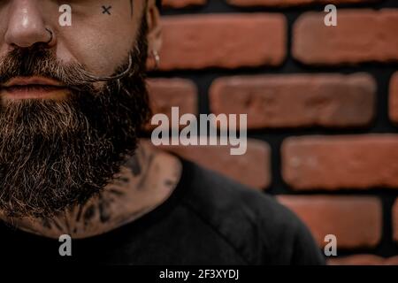 Primo piano di bello hipster vecchio-fashioned tatooed e trafitto su uno sfondo di mattone. Foto Stock
