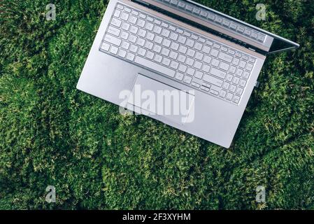 Laptop su erba verde, sfondo muschio. Viaggi ecologici, lavoro fuori ufficio concetto. Consapevolezza, design biofilo, concetto di scollegamento. Detox digitale Foto Stock