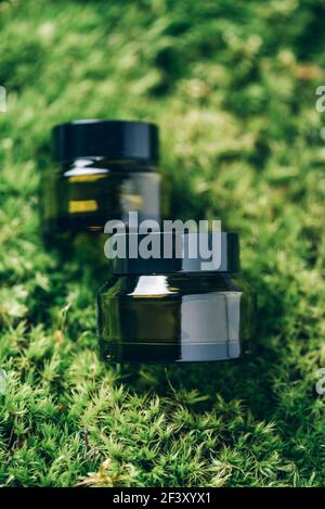 Contenitori per bottiglie in vetro verde per prodotti per la cura della pelle su erba, fondo muschio. Cura della pelle, cosmetici biologici, trattamento del corpo, concetto spa. Vegan eco Foto Stock
