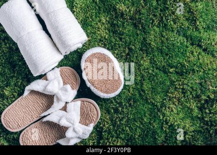 Spa, benessere, cura della pelle, concetto di bellezza e relax. Strumenti per il benessere: Asciugamano bianco, pantofole in bambù, pallina di erbe su erba verde, fondo muschio. Vista dall'alto Foto Stock