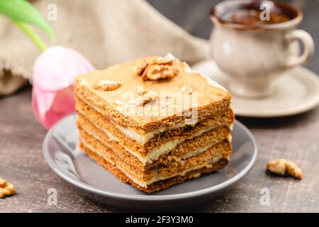 Fetta di torta al miele a strati su un piatto con tazza di caffè e tulipano fiore, fuoco selettivo Foto Stock