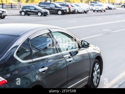 L'auto si muove su una strada a più corsie. Sul lato opposto della strada sono parcheggiate diverse auto. Foto Stock