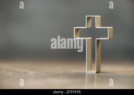 Silhouette di croce cristiana su sfondo grigio, bokeh morbido sfondo luci. Spazio di copia. Culto della Chiesa, concetto di salvezza. Simbolo della fede in Gesù Foto Stock