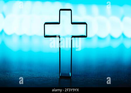 Silhouette di croce cristiana su sfondo blu, bokeh morbido sfondo luci. Spazio di copia. Culto della Chiesa, concetto di salvezza. Simbolo della fede in Gesù Foto Stock