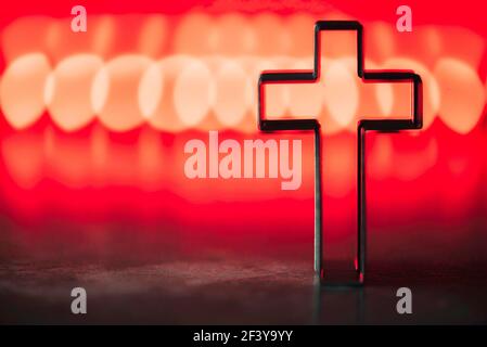 Silhouette di croce cristiana su sfondo rosso, bokeh morbido sfondo luci. Spazio di copia. Culto della Chiesa, concetto di salvezza. Simbolo della fede in Gesù Foto Stock