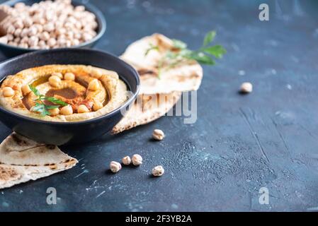 Hummus di ceci, olio d'oliva, ceci crudi, paprika affumicata, pita su fondo scuro. Cucina mediorientale, ebraica o arabica. Vista dall'alto. Copia Foto Stock