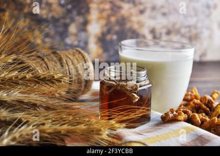 Aprire il vasetto in vetro di miele liquido, latte, noci, frumento sull'asciugamano vintage. Layout di sfondo con spazio di testo libero. Foto Stock