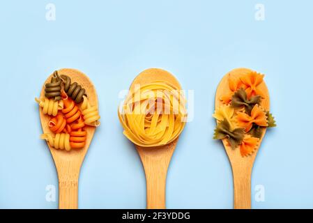 Diversi tipi di pasta cruda in tre cucchiai di legno su un blu sfondo Foto Stock