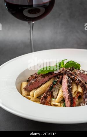 Con ​​grilleed di carne tagliata a fette su una cremosa pasta di penne. Foto Stock