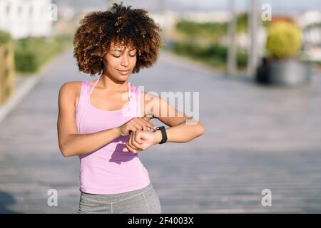Giovane donna nera utilizzando smartwatch toccando il touchscreen in active attività sportiva. Ragazza con i capelli afro guardando il suo orologio intelligente Schermo. Foto Stock