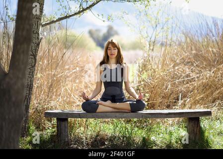 Giovane bella donna che fa yoga in natura. Giovane donna che fa yoga in natura. Donna che indossa abiti sportivi in figura di loto. Foto Stock