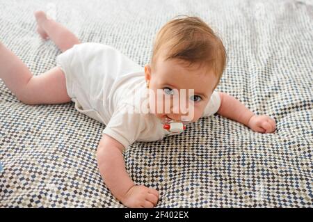 Happy Baby girl, quattro mesi, sul letto con succhietto. Foto Stock