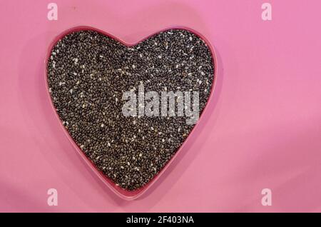 Semi di Chia a forma di cuore su sfondo rosa, vista dall'alto. Cibo sano, concetto di prodotto vegano Foto Stock