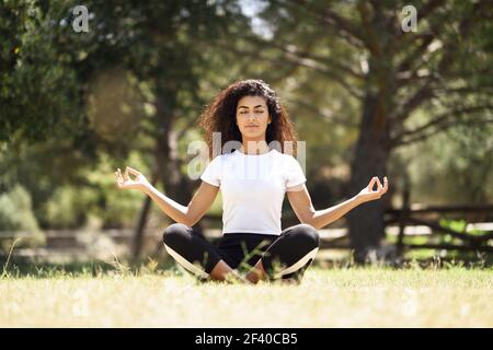 Giovane donna araba fare yoga in natura. Nord Africa indossando femmina sport vestiti facendo lotus figura nel parco urbano. Foto Stock