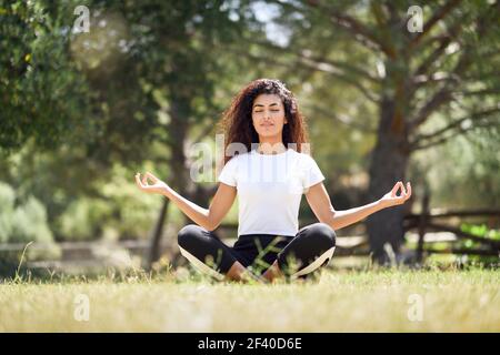 Giovane donna araba fare yoga in natura. Nord Africa indossando femmina sport vestiti facendo lotus figura nel parco urbano. Foto Stock