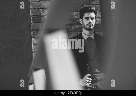 Uomo attraente per la strada che indossa un abito inglese elegante. Uomo d'affari giovane con acconciatura moderna in background urbano. Fotografia in bianco e nero. Foto Stock