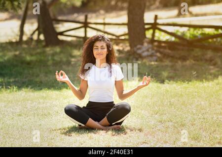 Giovane donna araba fare yoga in natura. Nord Africa indossando femmina sport vestiti facendo lotus figura nel parco urbano. Foto Stock