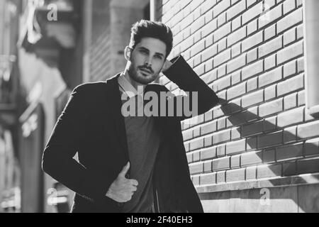 Uomo attraente per la strada che indossa un abito inglese elegante. Uomo d'affari giovane con acconciatura moderna in background urbano. Fotografia in bianco e nero. Foto Stock