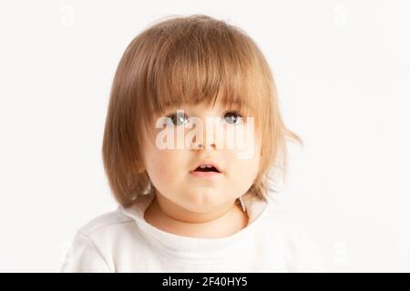 Primo piano di un bambino di 1 anno con un'espressione facciale sorpresa su sfondo bianco. Foto Stock