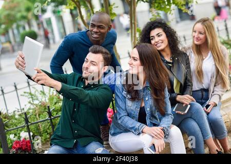 Gruppo multietnico di giovani che fotografano selfie insieme all'aperto. Belle donne e uomini divertenti che indossano abiti casual in background urbano. Giovani multietnici che si riuniscono selfie in un contesto urbano Foto Stock