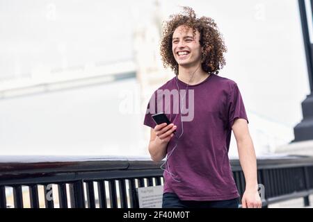 Giovane che ascolta la musica con auricolari e phon intelligente in ambiente urbano. Tamigi a Londra. Uomo che ascolta la musica in ambiente urbano. Foto Stock