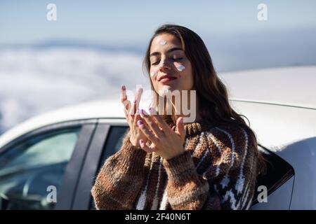 Giovane donna che applica la protezione solare sul viso in montagne innevate in inverno, in Sierra Nevada, Granada, Spagna. Donna che indossa abiti invernali.. Giovane donna che applica la protezione solare sul suo viso in paesaggio di neve Foto Stock