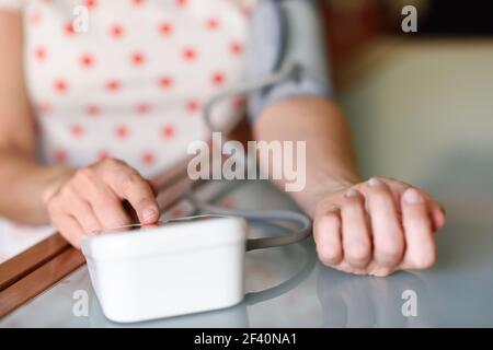 Donna di mezza età che misura la propria pressione sanguigna con un dispositivo elettronico per la misurazione della pressione sanguigna a casa. Donna che misura la propria pressione sanguigna a casa. Foto Stock