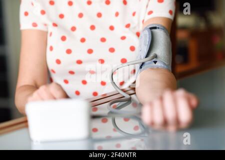 Donna di mezza età che misura la propria pressione sanguigna con un dispositivo elettronico per la misurazione della pressione sanguigna a casa. Donna che misura la propria pressione sanguigna a casa. Foto Stock