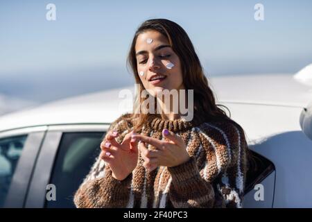 Giovane donna che applica la protezione solare sul viso in montagne innevate in inverno, in Sierra Nevada, Granada, Spagna. Donna che indossa abiti invernali.. Giovane donna che applica la protezione solare sul suo viso in paesaggio di neve Foto Stock