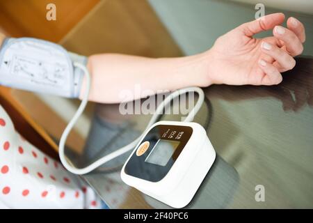 Donna di mezza età che misura la propria pressione sanguigna con un dispositivo elettronico per la misurazione della pressione sanguigna a casa. Donna che misura la propria pressione sanguigna a casa. Foto Stock