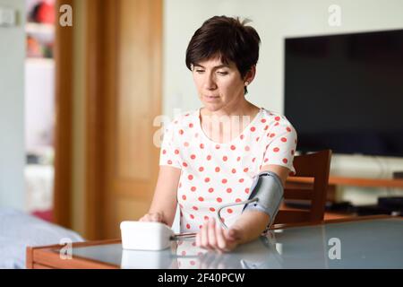 Donna di mezza età che misura la propria pressione sanguigna con un dispositivo elettronico per la misurazione della pressione sanguigna a casa. Donna che misura la propria pressione sanguigna a casa. Foto Stock