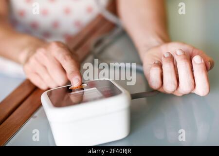 Donna di mezza età che misura la propria pressione sanguigna con un dispositivo elettronico per la misurazione della pressione sanguigna a casa. Donna che misura la propria pressione sanguigna a casa. Foto Stock