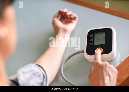 Donna di mezza età che misura la propria pressione sanguigna con un dispositivo elettronico per la misurazione della pressione sanguigna a casa. Donna che misura la propria pressione sanguigna a casa. Foto Stock