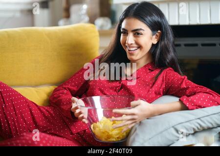 Donna persiana a casa guardando la TV. Ragazza mangiare patatine patate. Donna persiana a casa guardando la TV mangiare patate chips Foto Stock