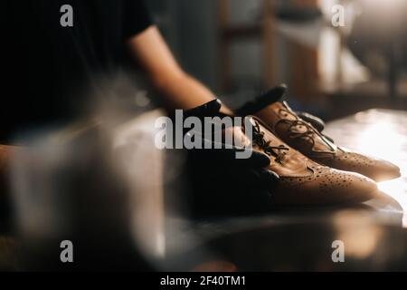 Vista laterale ravvicinata delle mani del calzolaio nero guanti che tengono vecchie scarpe in pelle marrone chiaro Foto Stock