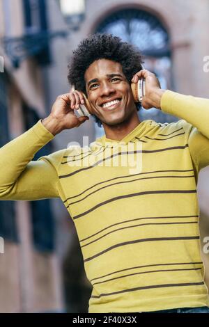 Uomo nero con capelli afro ascolto di musica con cuffie wireless visite turistiche a Granada, Andalusia, Spagna.. Uomo nero che ascolta la musica con le cuffie wireless per visitare Granada Foto Stock