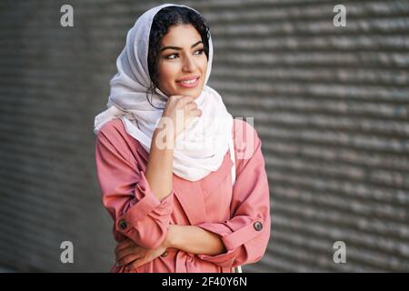 Donna musulmana sorridente con foulard hijab che cammina nel centro della città. Donna araba in ambiente urbano. Giovane donna araba con foulard hijab che cammina nel centro della città. Foto Stock