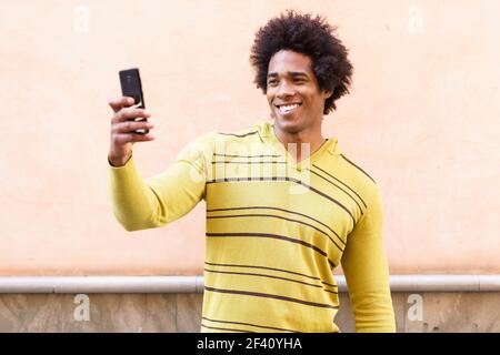 Uomo nero con capelli afro e cuffie utilizzando smartphone per scattare fotografie. Uomo nero con capelli afro e cuffie con smartphone. Foto Stock