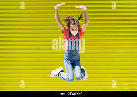 Happy Child ragazza saltando indossando una maschera di protezione contro il coronavirus durante la pandemia di Covid-19. Maschera KN95. Bambina saltando indossando una maschera di protezione contro il coronavirus Foto Stock