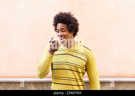 Uomo nero con capelli afro e cuffie con smartphone che invia una nota vocale. Uomo nero con capelli afro e cuffie con smartphone. Foto Stock